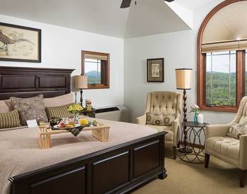Dark wood grand bed frame with head and footboard. Two striped wing back chairs with two windows with a vew
